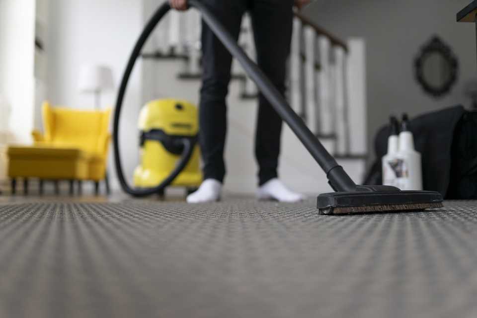 vacuuming gray patterned carpet in modern living room with yellow armchair